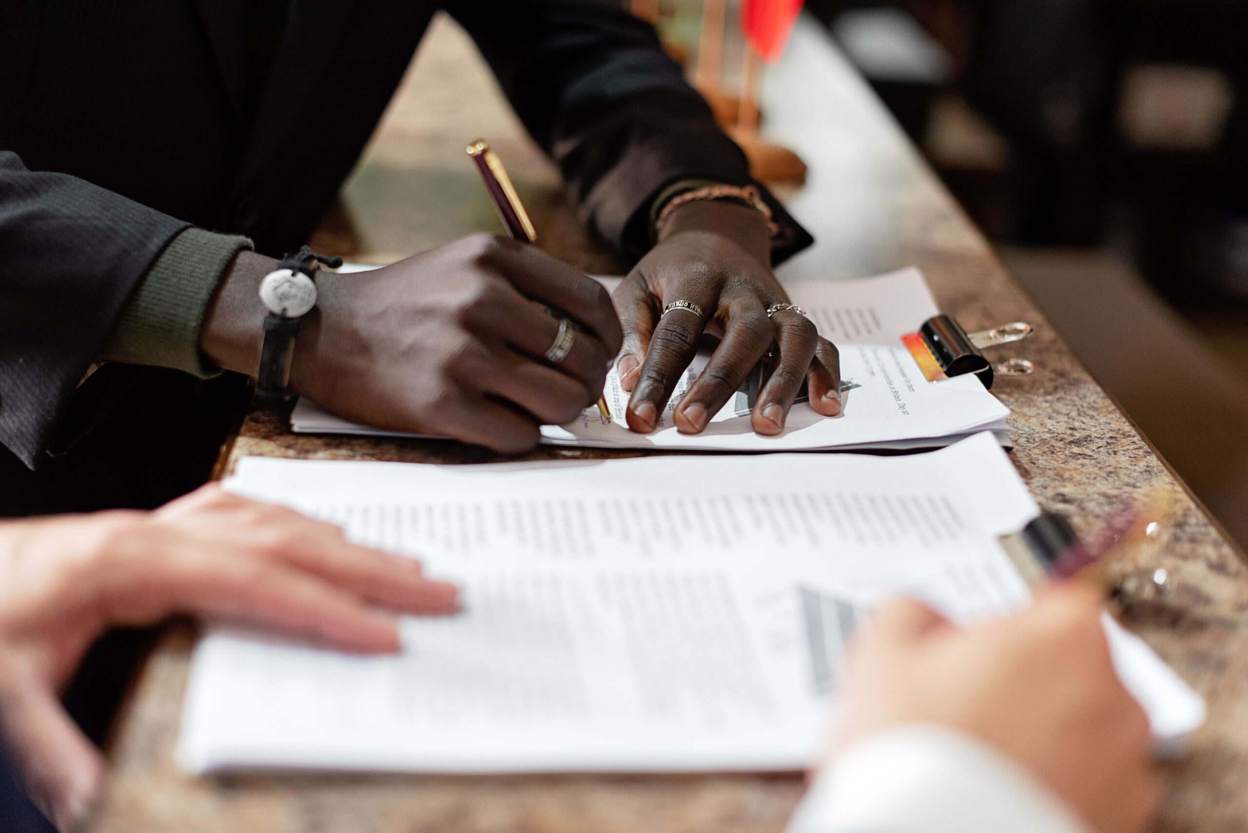 Close-up of hands signing documents in a business setting, emphasizing professionalism and teamwork.